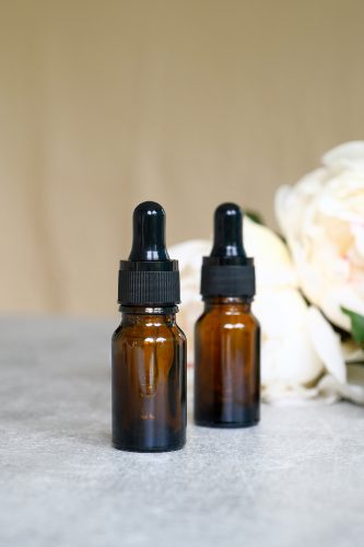 Amber glass dropper bottles mockup and peony flowers on stone table. Herbal cosmetic, natural organic beauty product, essential oil packaging design.